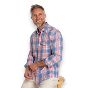 Close-up of a person's chest in the CRIQUET - DOUBLE CLOTH FLANNEL PEARL SNAP SHIRT IN SUNSET, a blue, white, and orange plaid flannel with pearl snaps, front pocket with flap, and visible chest hair at the open collar.