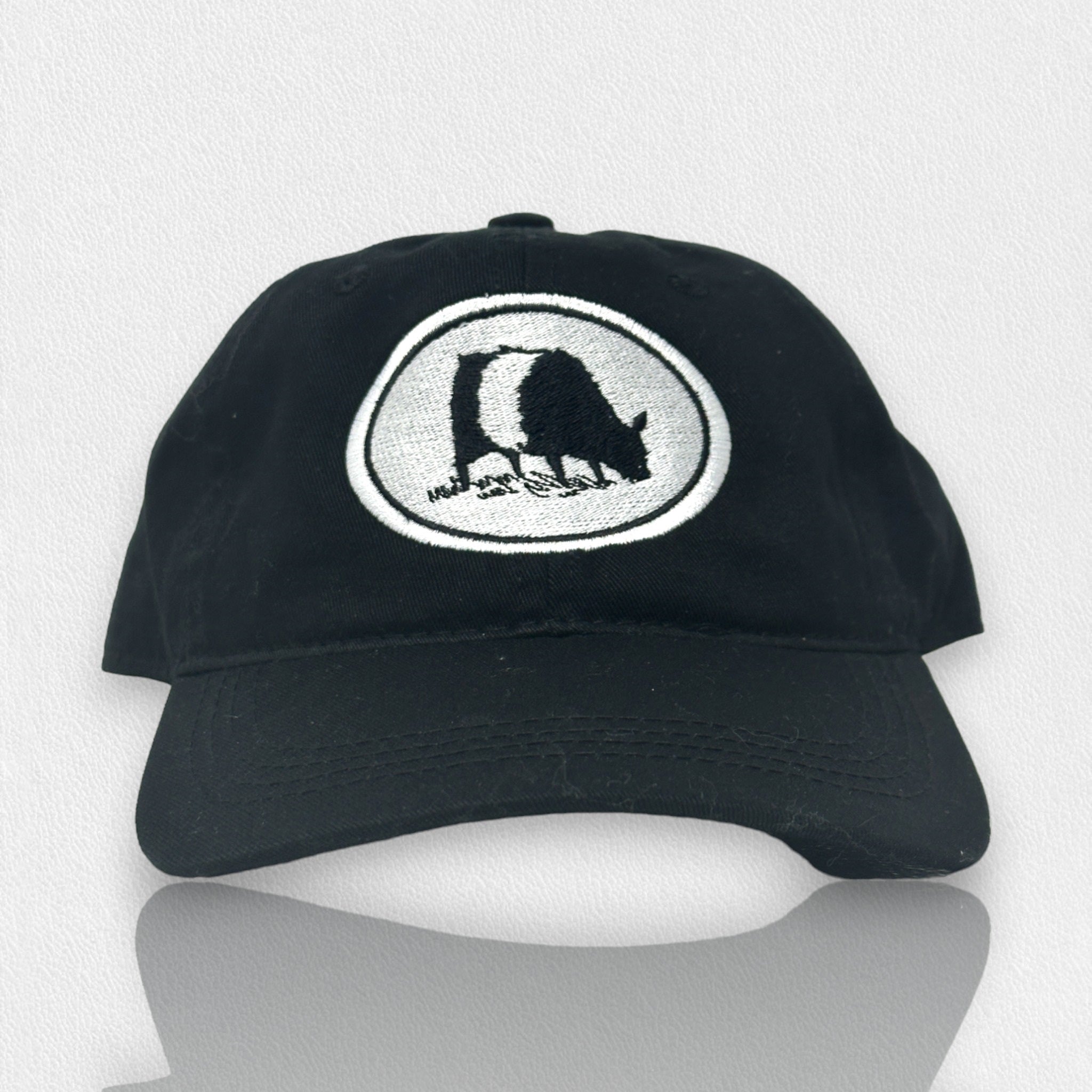 A black baseball cap with a white oval patch showing a black-and-white illustration of a bear walking, stitched on the front. The cap is displayed against a light, textured background.
