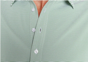 A man wears the CRIQUET Performance Sport Range Polo in Hobby Stripe - Gator, featuring light green and white stripes, a collar, and buttons, standing with one hand in his pocket against a plain background.