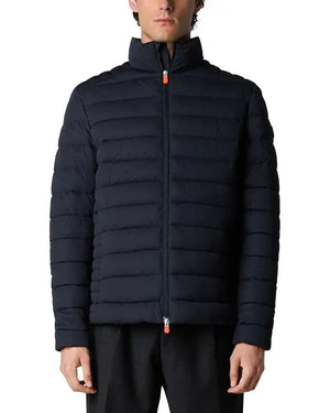 Someone stands against a plain white background wearing the SAVE THE DUCK - ARI PUFFER JACKET, a dark blue, quilted sustainable jacket by SAVE THE DUCK with a high collar and front zipper.