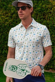 A man wears the CRIQUET Performance Sport Range Polo in white with a blue and yellow pickleballer print, standing against a plain background. This breathable men's polo is perfect for golf or any occasion.