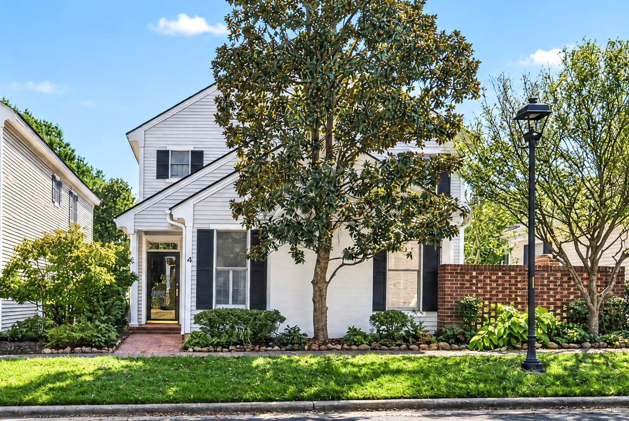 A two-story white house with black shutters, a front door with a glass pane, and a large tree in the front yard.