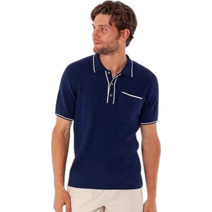 A man models the CRIQUET Bungalow Sweater Polo in navy, featuring white trim on the collar, sleeve cuffs, buttons, and pocket, against a plain white background.