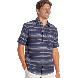 A man smiles with one hand in his pocket, wearing the CRIQUET Hemp Stripe Pearl Snap Shirt in Navy—short-sleeve, button-up with white stripes—paired with beige pants.