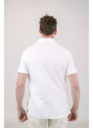 A man with light brown hair and a short beard wears the EDWARD ARMAH Pima Cotton Tailored Polo Shirt in dark blue and jeans, standing against a plain light background with a relaxed expression and one hand in his pocket.