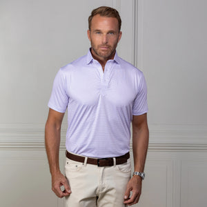 A man with short light brown hair and a beard wears the COLLARS AND CO - FEATHERWEIGHT FLEX POLO MACKENZIE, beige pants, and a brown belt, standing against a light-colored paneled wall.