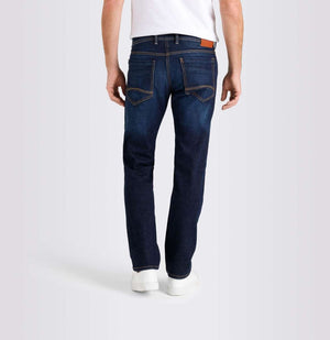 A person wearing MAC JEANS - BEN AUTHENTIC DENIM REGULAR FIT DARK VINTAGE WASH by MAC, paired with a white t-shirt and white sneakers, stands against a plain light gray background.