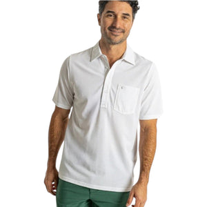 A man with dark hair and a short beard wears the CRIQUET Oxford Pique Players Shirt in white and green shorts, standing against a plain white background and smiling.
