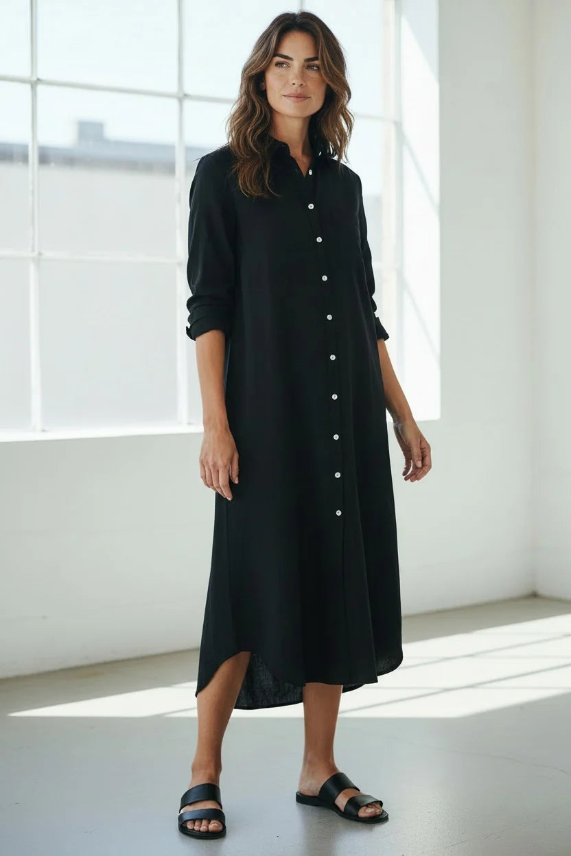 A woman wearing a long-sleeved black button-down midi shirt dress and black slide sandals.