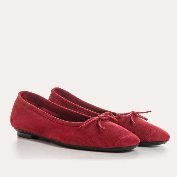 A person wearing blue jeans and REQINS - HARMONY Suede Ballerina Flats in cerise stands on a light-colored floor.