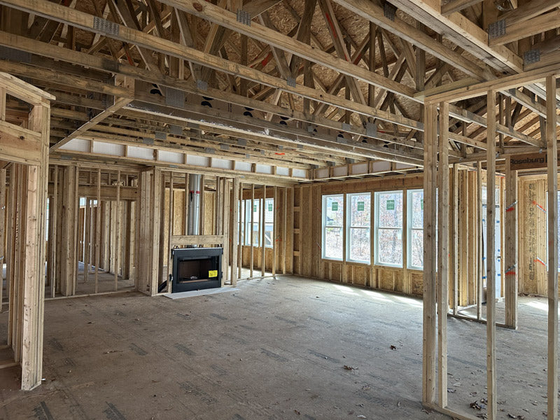 Wood framing of a house under construction with exposed beams, unfinished walls, a fireplace installed, and several windows allowing natural light into the open space.