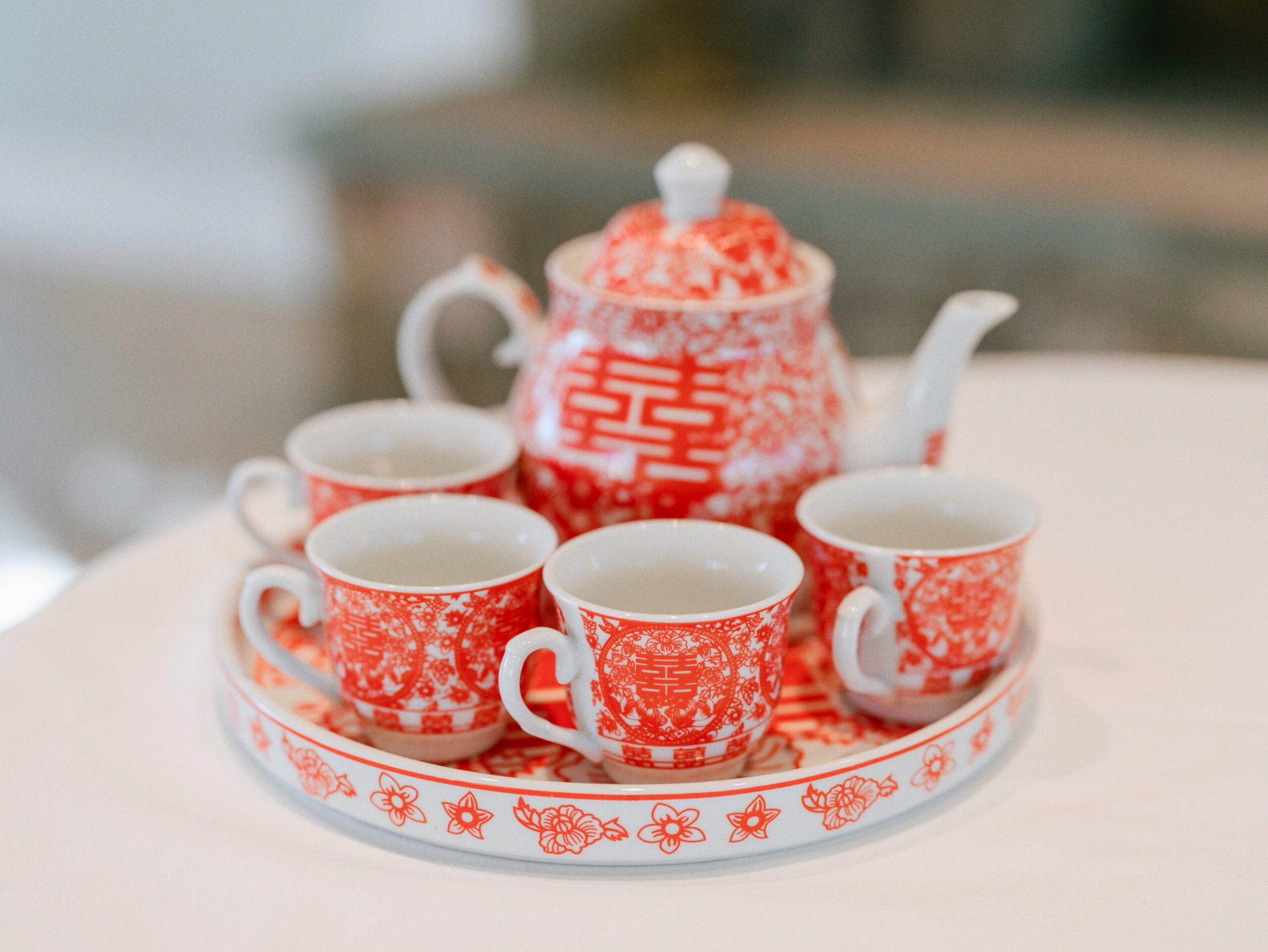 A white and red ceramic tea set with a teapot, four teacups, and a round tray featuring floral and geometric patterns, arranged neatly on a white surface.