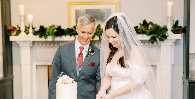 Couple in wedding attire standing in front of a fireplace with a cake.