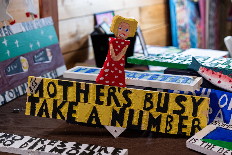 A handmade wooden sign with a painted figure of a blonde woman in a red dress and the words