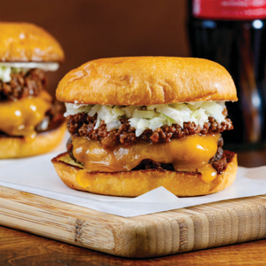 A woman in a light sweater selects fresh tomatoes at an outdoor market, holding a colorful basket. The cover reads: "Spring Council, Southern Roots Buffet Luncheon, Feb 13, 2026—FEARRINGTON VILLAGE.