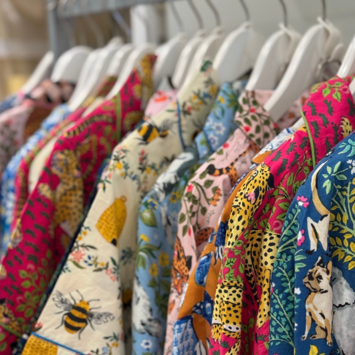 A row of colorful, patterned shirts on white hangers, featuring various animal and nature designs such as bees, leopards, birds, and foliage. The shirts are displayed closely together on a clothing rack.