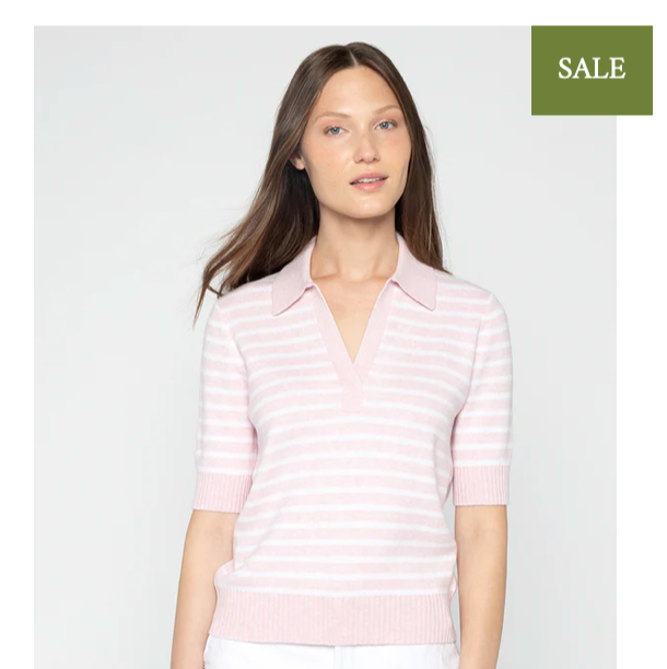 A woman wearing a light pink and white striped short-sleeve sweater with a collar stands against a plain background. A green