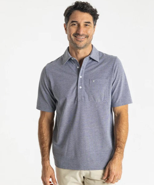 Close-up of a person wearing the CRIQUET Oxford Pique Players Shirt in First Mate, featuring blue textured fabric, white buttons, a chest pocket with a small embroidered logo.