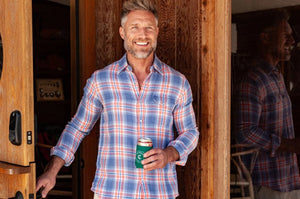 Close-up of a person's chest in the CRIQUET - DOUBLE CLOTH FLANNEL PEARL SNAP SHIRT IN SUNSET, a blue, white, and orange plaid flannel with pearl snaps, front pocket with flap, and visible chest hair at the open collar.