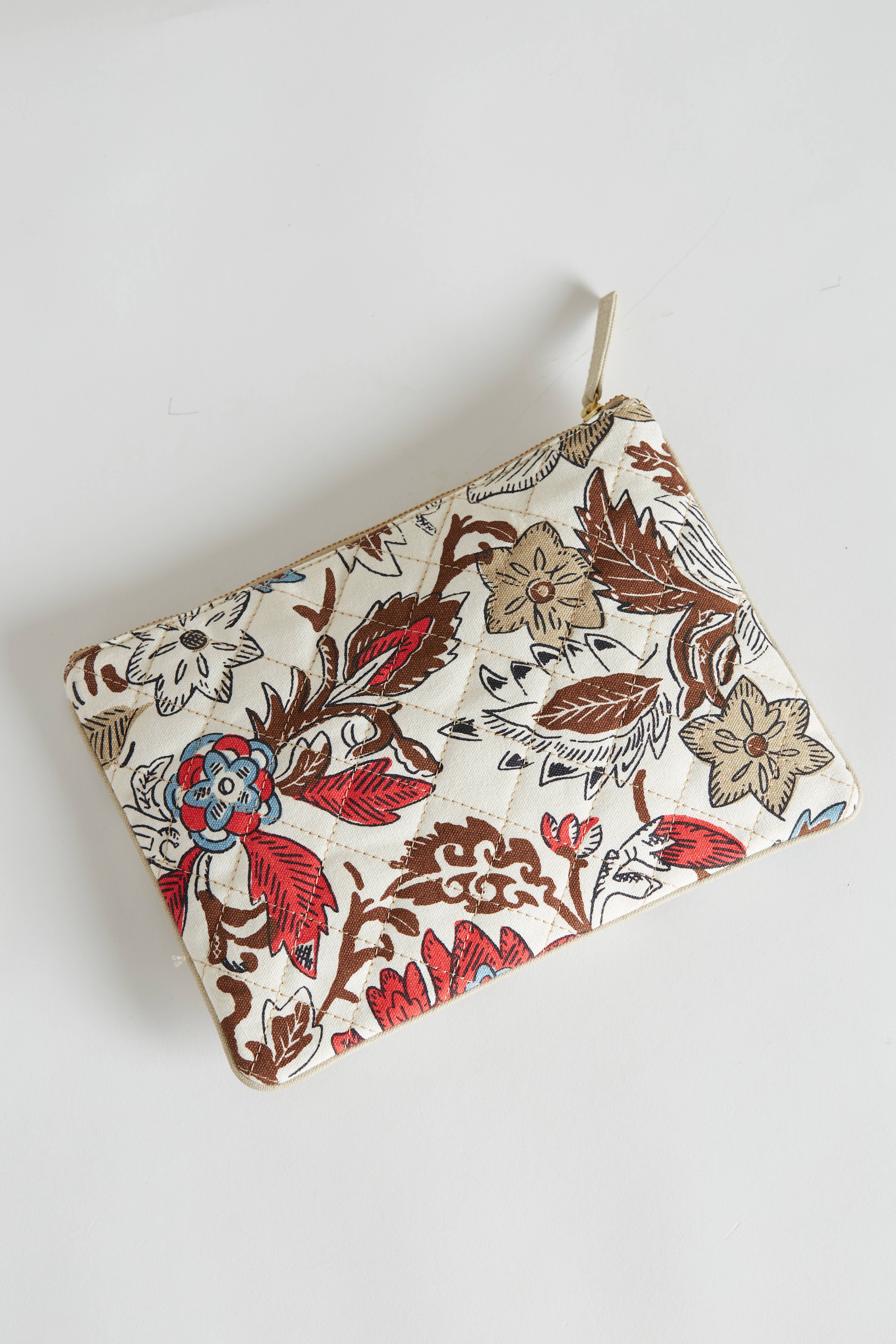 A rectangular fabric pouch with a zipper, featuring a floral pattern in red, brown, blue, and beige on a white background, placed on a white surface.