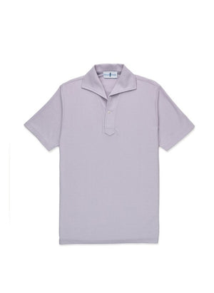 A man with light brown hair and a short beard wears the EDWARD ARMAH Pima Cotton Tailored Polo Shirt in dark blue and jeans, standing against a plain light background with a relaxed expression and one hand in his pocket.