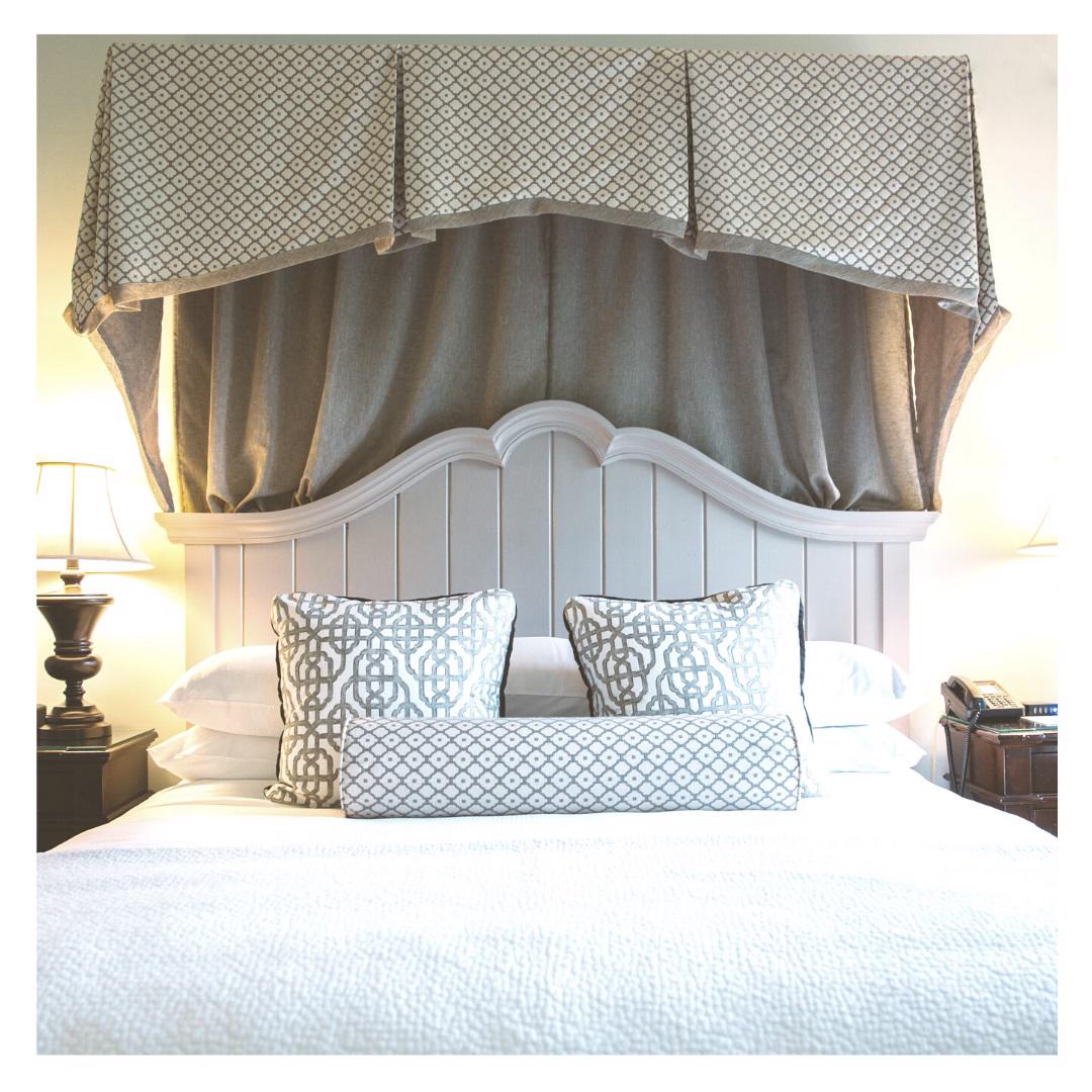 A perfectly made bed with the FEARRINGTON HOUSE Fearrington Lifestyle Bedding Collection – Ultimate King Sleep Experience, patterned pillows, a matching canopy, and bedside tables with lamps set against a light headboard.