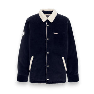 The AMUNDSEN SPORTS Harvester Overshirt in True Navy is a stretch cotton corduroy jacket with white sherpa trim, chest and side pockets, snap buttons, and a circular left-sleeve patch.