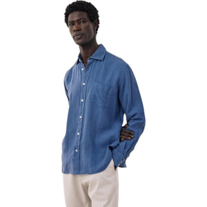 A person with short, curly black hair is seen from behind wearing the HARTFORD - PAUL Linen Shirt in Denim by HARTFORD, set against a plain light background.