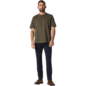 A man with short hair and a beard stands facing forward, wearing an olive green T-shirt, 34 HERITAGE - COURAGE STRAIGHT LEG PANT IN NAVY TWILL, and brown shoes against a plain white background.