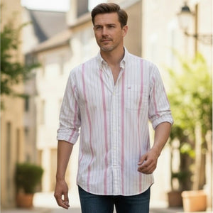 A man in a FRANK & EILEEN FINBAR men's button-up shirt in hot pink and blue stripe, paired with jeans, walks outdoors along a sunlit street lined with buildings and greenery.