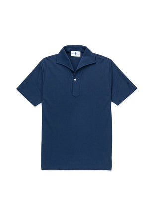 A man with light brown hair and a short beard wears the EDWARD ARMAH Pima Cotton Tailored Polo Shirt in dark blue and jeans, standing against a plain light background with a relaxed expression and one hand in his pocket.