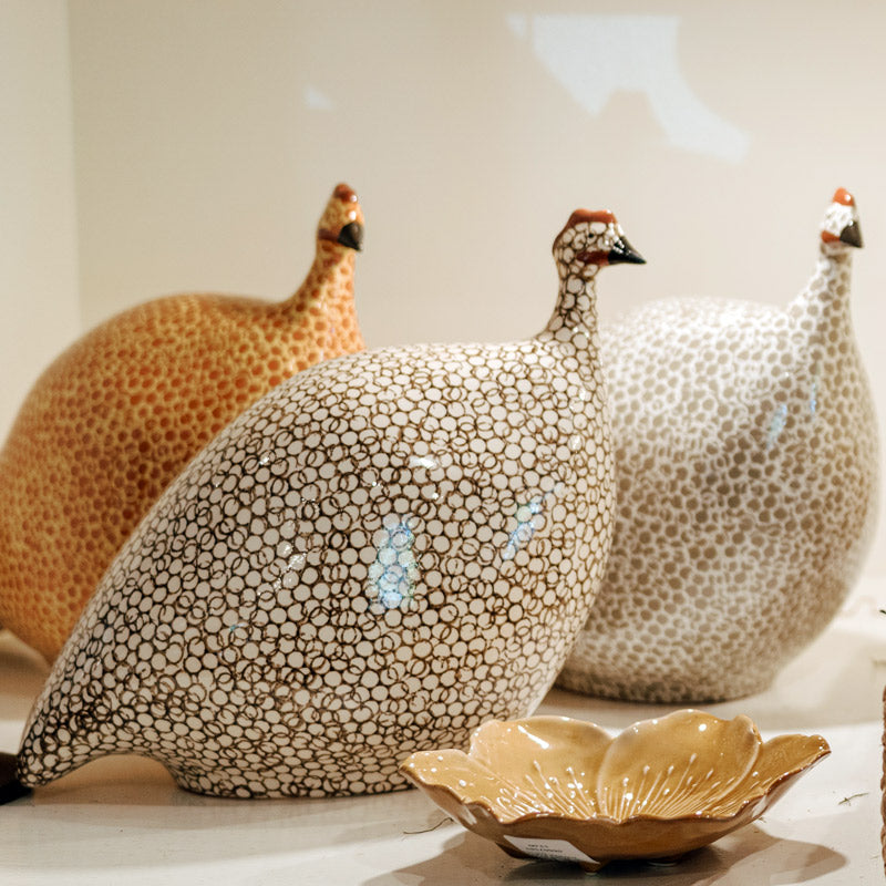 Three ceramic sculptures of guinea fowl with spotted patterns in shades of brown, white, and orange are displayed together, with a leaf-shaped dish in the foreground.