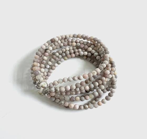 A multi-strand beaded bracelet made of round, smooth, light pink and gray beads with a silver clasp, coiled neatly on a white background.