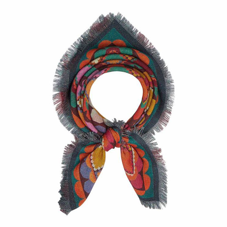 A colorful, fringed scarf is tied in a loose knot. The scarf features a vibrant, retro pattern with orange, red, yellow, purple, and green scalloped shapes. The edges are frayed, adding texture to the design.
