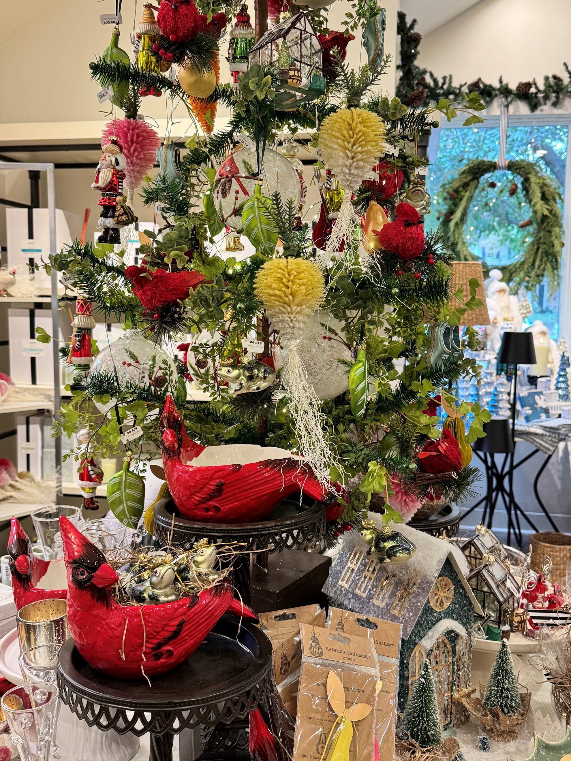 A festive display features a decorated Christmas tree with red bird ornaments, yellow and white decorations, and artificial greenery. Red bird figurines and various holiday items are arranged on the table below the tree.
