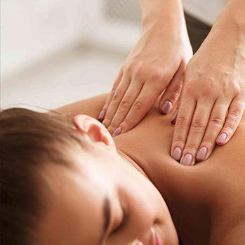 A person receiving a relaxing back massage, with two hands gently pressing on their upper back and shoulders in a calm, softly lit environment.