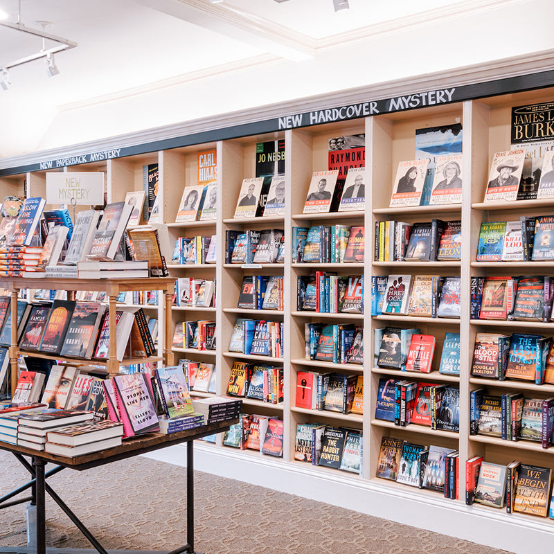 Bookshelves and a display table filled with various new hardcover mystery books in a well-lit bookstore section labeled