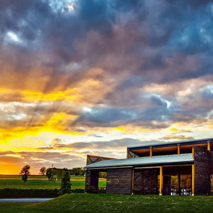 A metal sign reading "red tail ridge" with a tree and bird sculpture stands on grass at sunset—an inviting welcome to the Red Tail Ridge Wine Dinner by FEARRINGTON VILLAGE, perfect for a Finger Lakes wine experience.