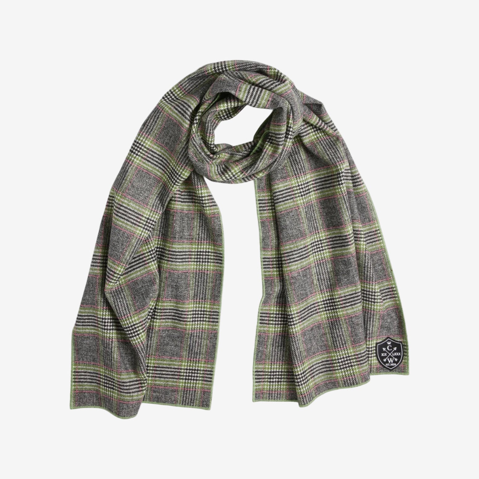 A wool scarf with a gray, black, and green plaid pattern, loosely draped in a loop. It features a small black patch with white text and graphics stitched on one end.