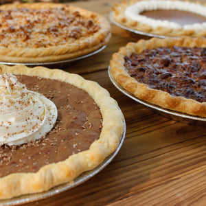 A fruit pie and a crumb-topped Thanksgiving Pies - Pickup November 26, 2026 on a wooden table outdoors.