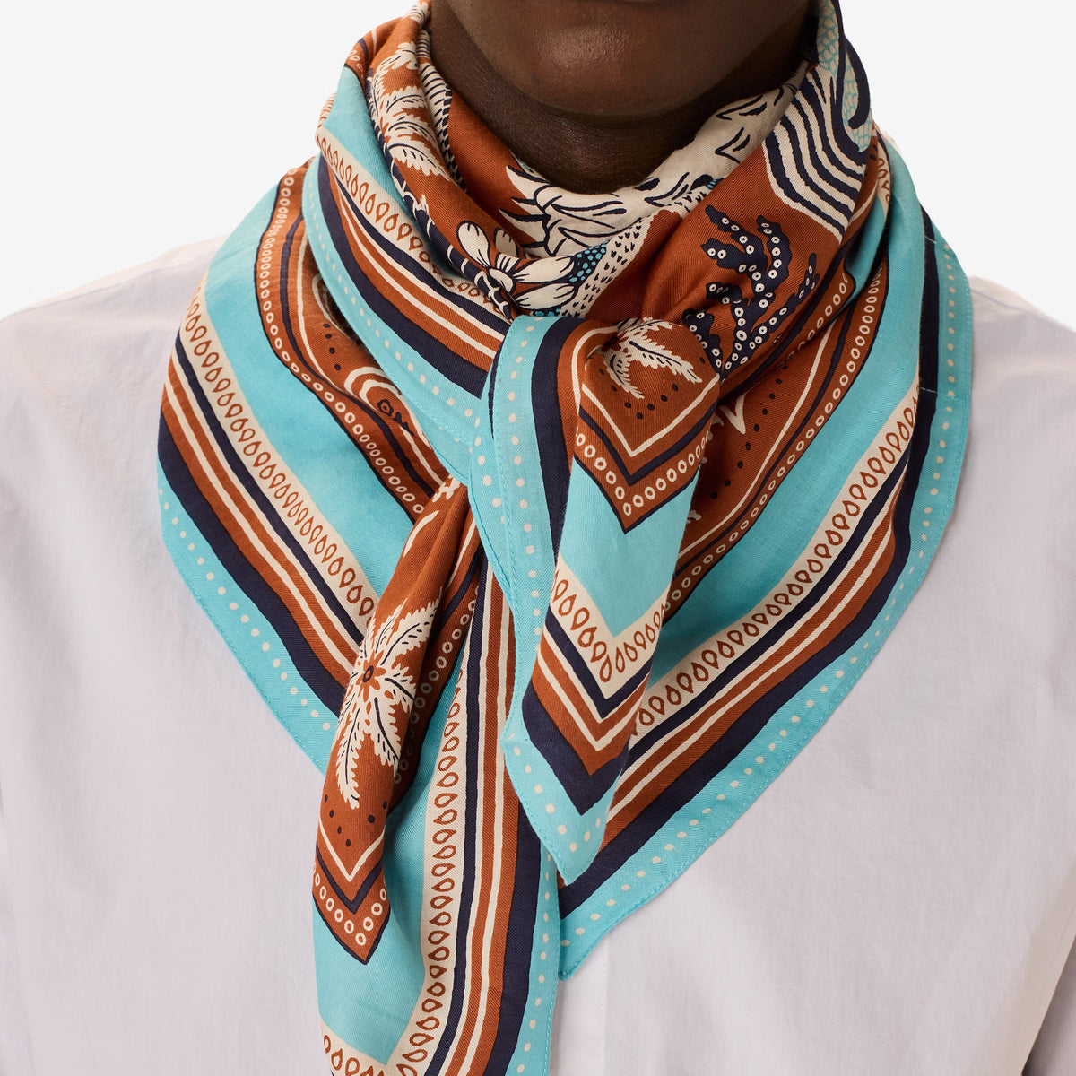 The INOUI EDITIONS - NEPTUNE SCARF IN GOLDEN BROWN by INOUI features detailed blue and white tropical fish, seaweed, shells, and coral on a brown background with an intricate blue, white, and brown border in cotton silk.