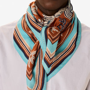 The INOUI EDITIONS - NEPTUNE SCARF IN GOLDEN BROWN by INOUI features detailed blue and white tropical fish, seaweed, shells, and coral on a brown background with an intricate blue, white, and brown border in cotton silk.