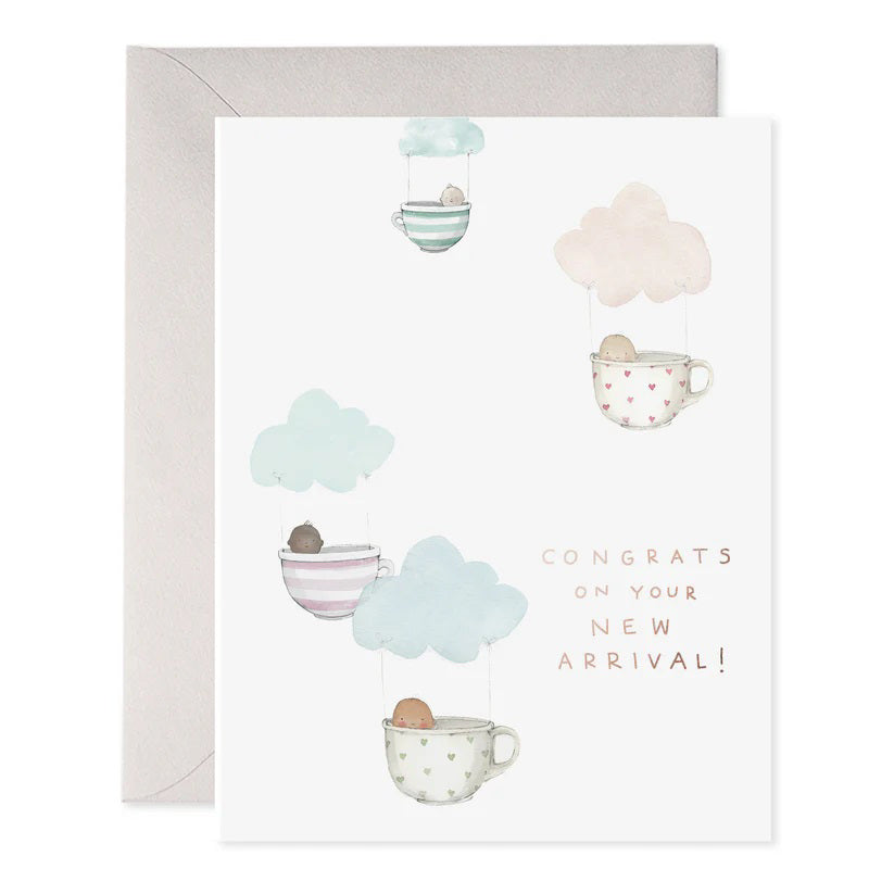 The E. FRANCES PAPER - TEACUP BABIES GREETING CARD features a watercolor painting of four teacups beneath pastel clouds, each holding a small brown object, with "Congrats on your new arrival!" text. It's elegantly paired with a gray envelope.