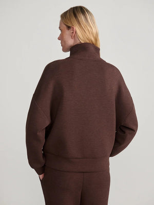A person wears an oversized, dark brown VARLEY - HAWLEY HALF-ZIP SWEATSHIRT IN COFFEE BEAN MARL with a gold zipper.