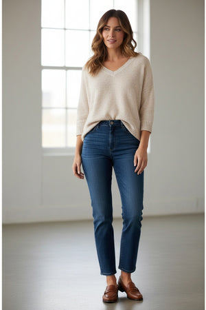 A woman with light hair wears the BASE MILANO V NECK COTTON SWEATER in light beige, styled with blue jeans, against a simple light background.
