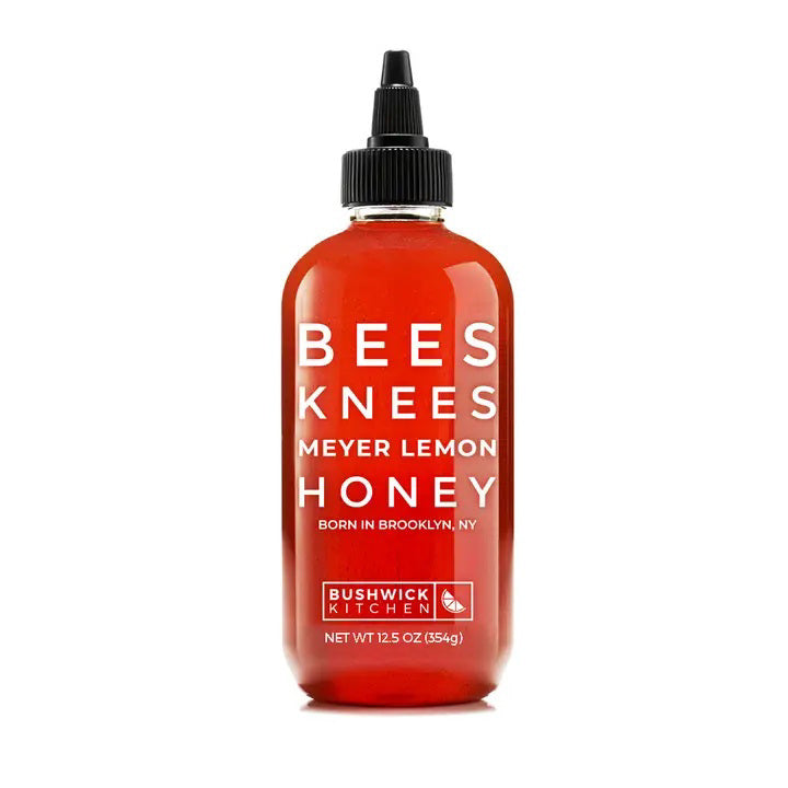 A 12.5 oz (354g) bottle of BUSHWICK KITCHEN - 'BEES KNEES' MEYER LEMON HONEY features a black nozzle cap and is filled with citrus-infused honey. The red label with white text displays the brand name, BUSHWICK KITCHEN, and product name while indicating its origin in Brooklyn, NY.