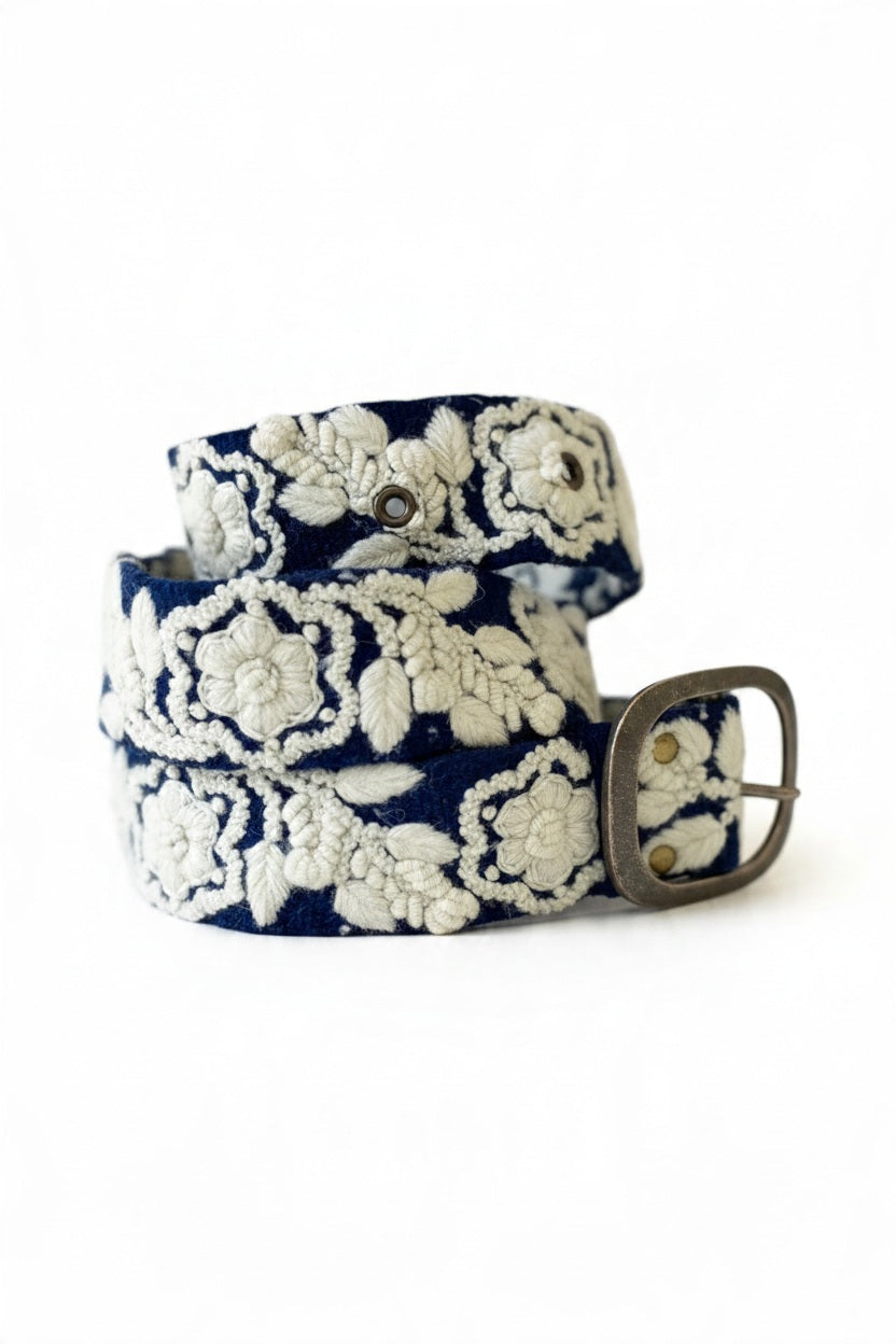 The JENNY KRAUSS Two Toned Belted in Blue and Cream features intricate embroidery, a silver rectangular buckle, and is handcrafted in Peru. Shown coiled on a white surface.