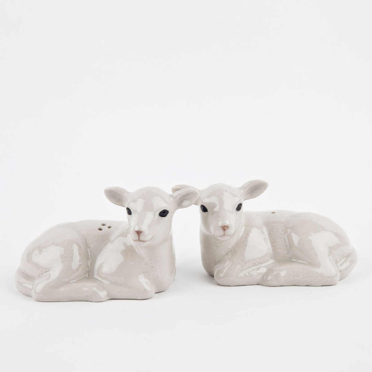 The QUAIL CERAMICS Lamb Salt and Pepper Set by QUAIL DESIGNS features two hand-painted stoneware shakers, shaped like resting lambs in white and pale gray, displayed side by side on a plain white background.