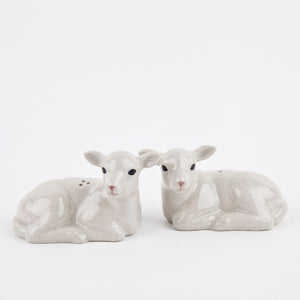 The QUAIL CERAMICS Lamb Salt and Pepper Set by QUAIL DESIGNS features two hand-painted stoneware shakers, shaped like resting lambs in white and pale gray, displayed side by side on a plain white background.