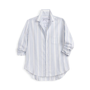 A woman smiles over her shoulder in a bright kitchen, wearing the FRANK & EILEEN EILEEN Relaxed Button Up Shirt in Italian Flannel Blue Stripe, paired with blue jeans for an effortless, breezy look.